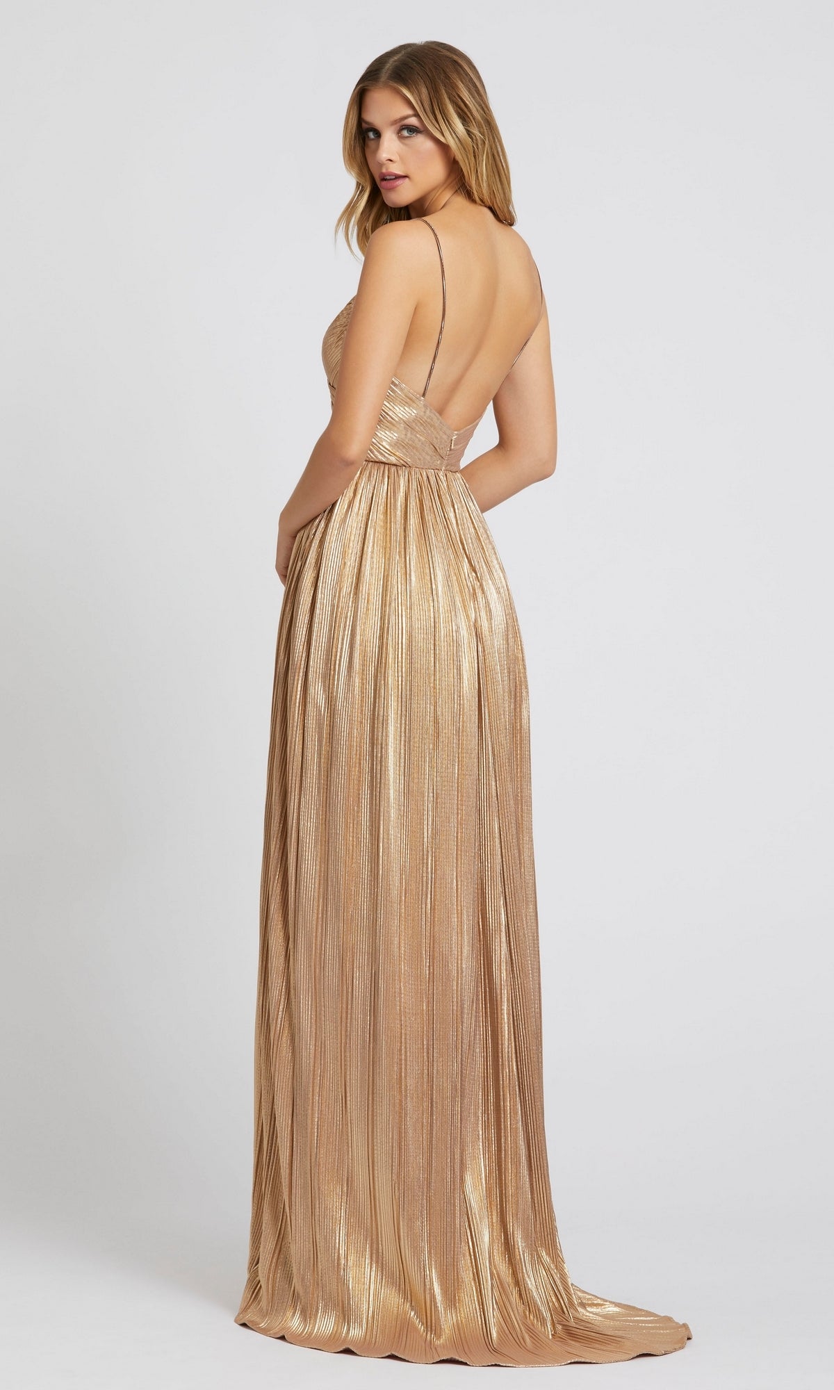 A woman wears the Mac Duggal 26275 Long Gold Pleated Formal Dress, featuring thin straps and an open back, shimmering in metallic gold against a plain light background.